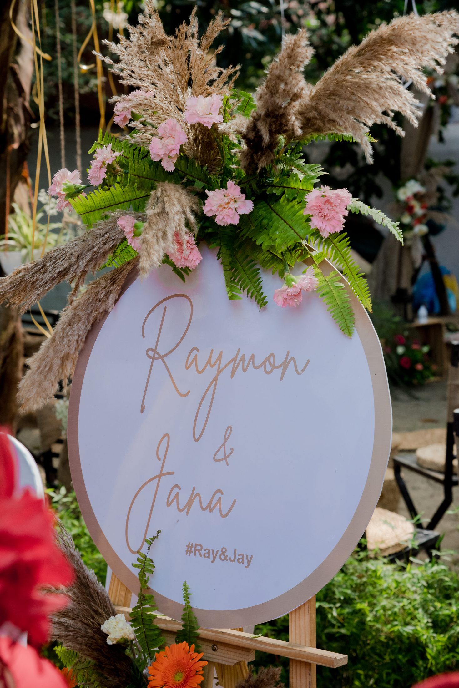 Floral welcome sign reading Raymon and Jana with pampas grass and pink flowers