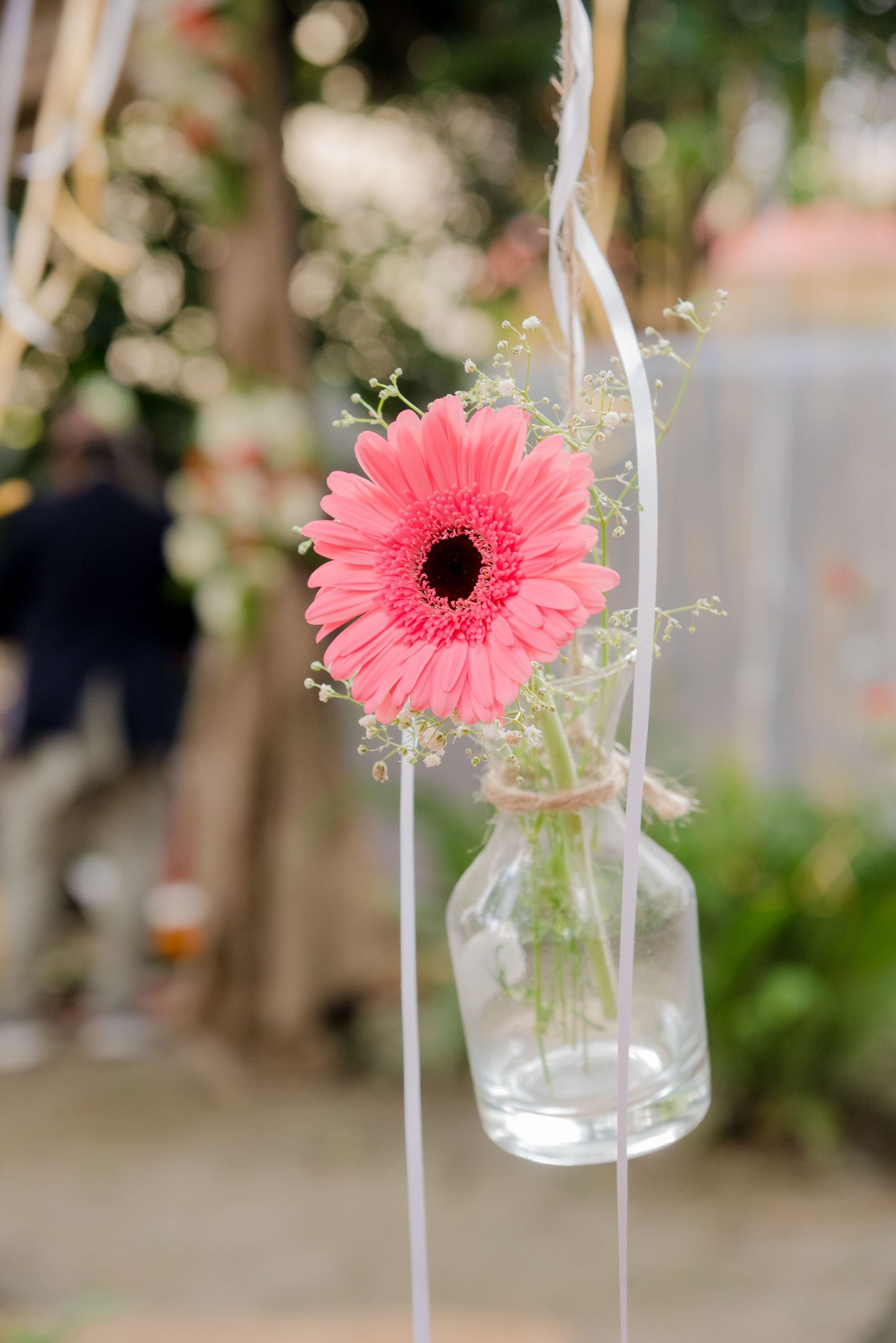 Pink gerbera daisy in a hanging glass bottle vase decorating the venue
