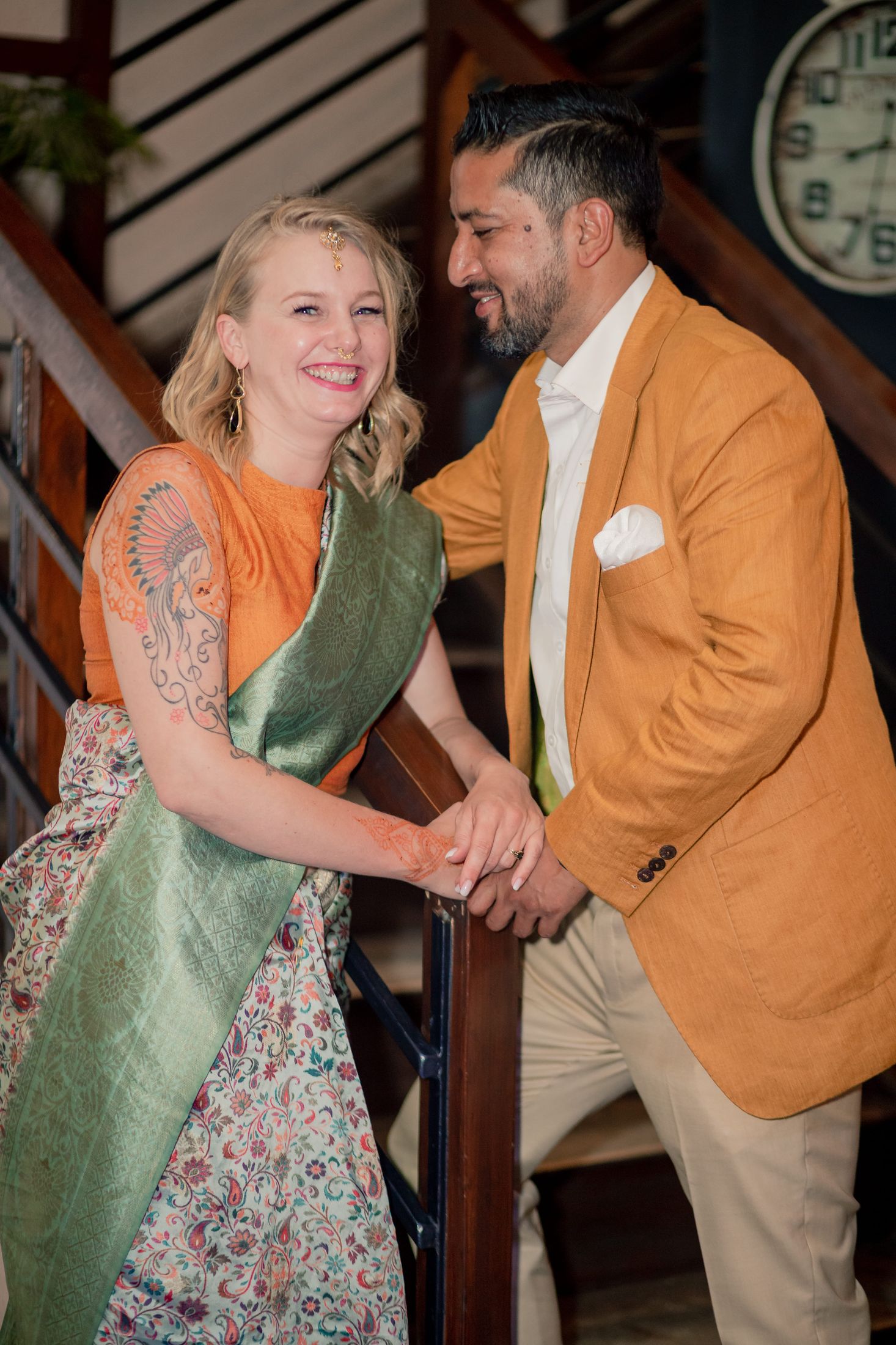 Jana and Raymon looking closely at each other on a staircase, she in an orange and green outfit