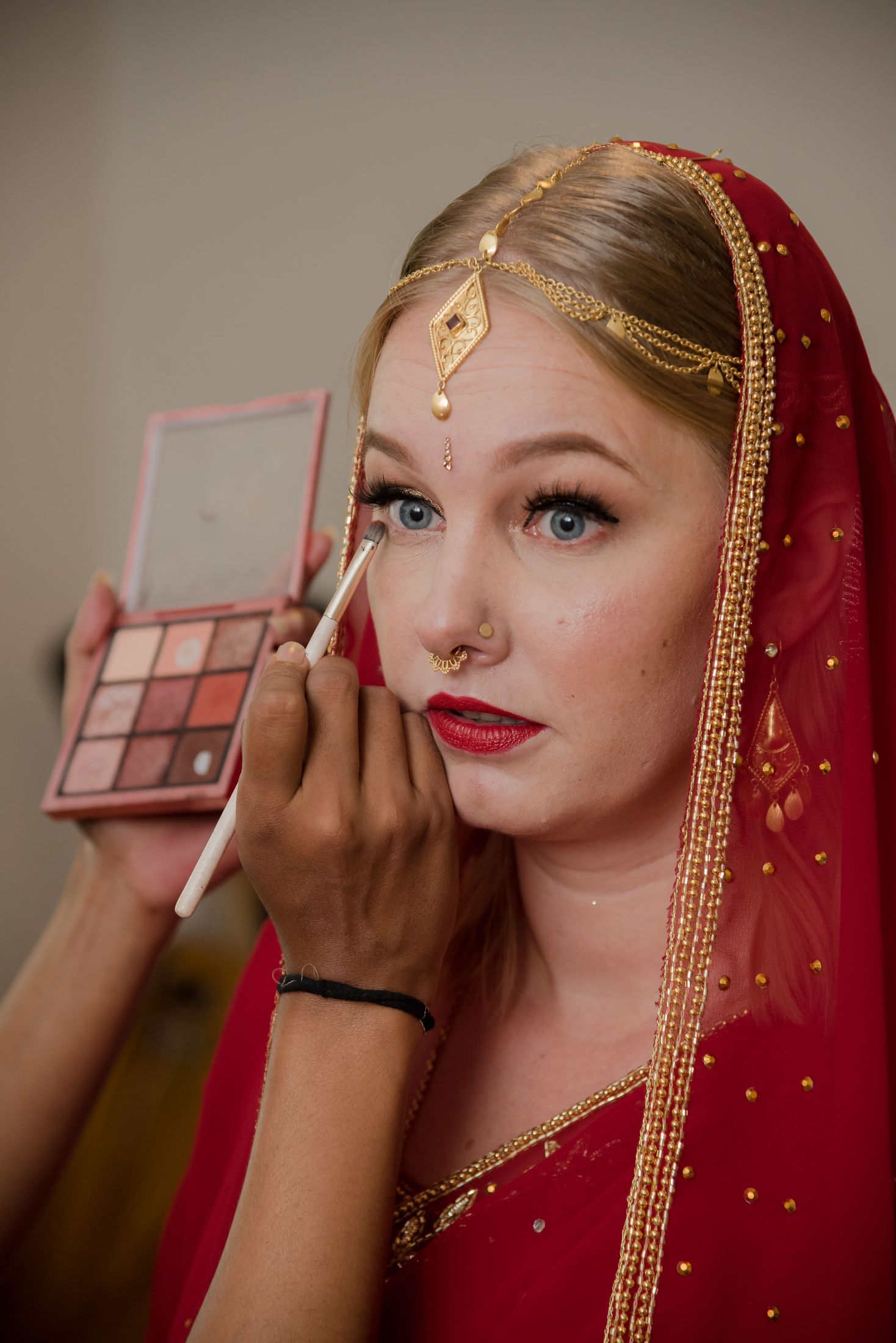 Jana in a red bridal veil and gold headpiece having her makeup applied