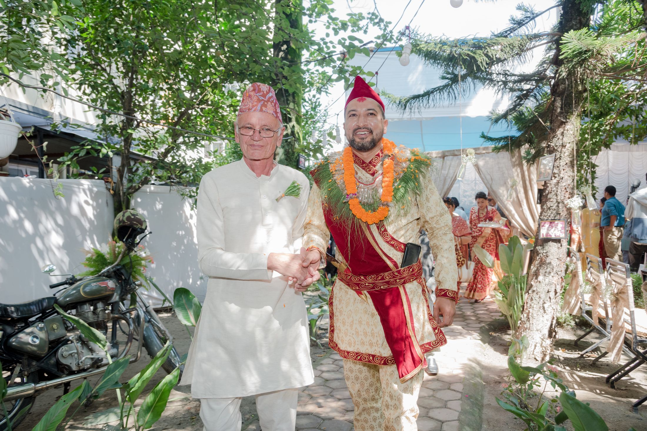 Raymon walking with an older man in a white kurta and Nepali topi during the wedding procession