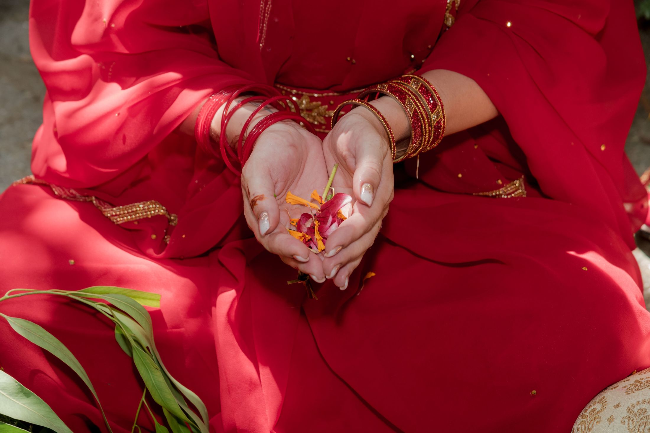 Close-up of Jana's hands cupped with flower petals, wearing red bangles
