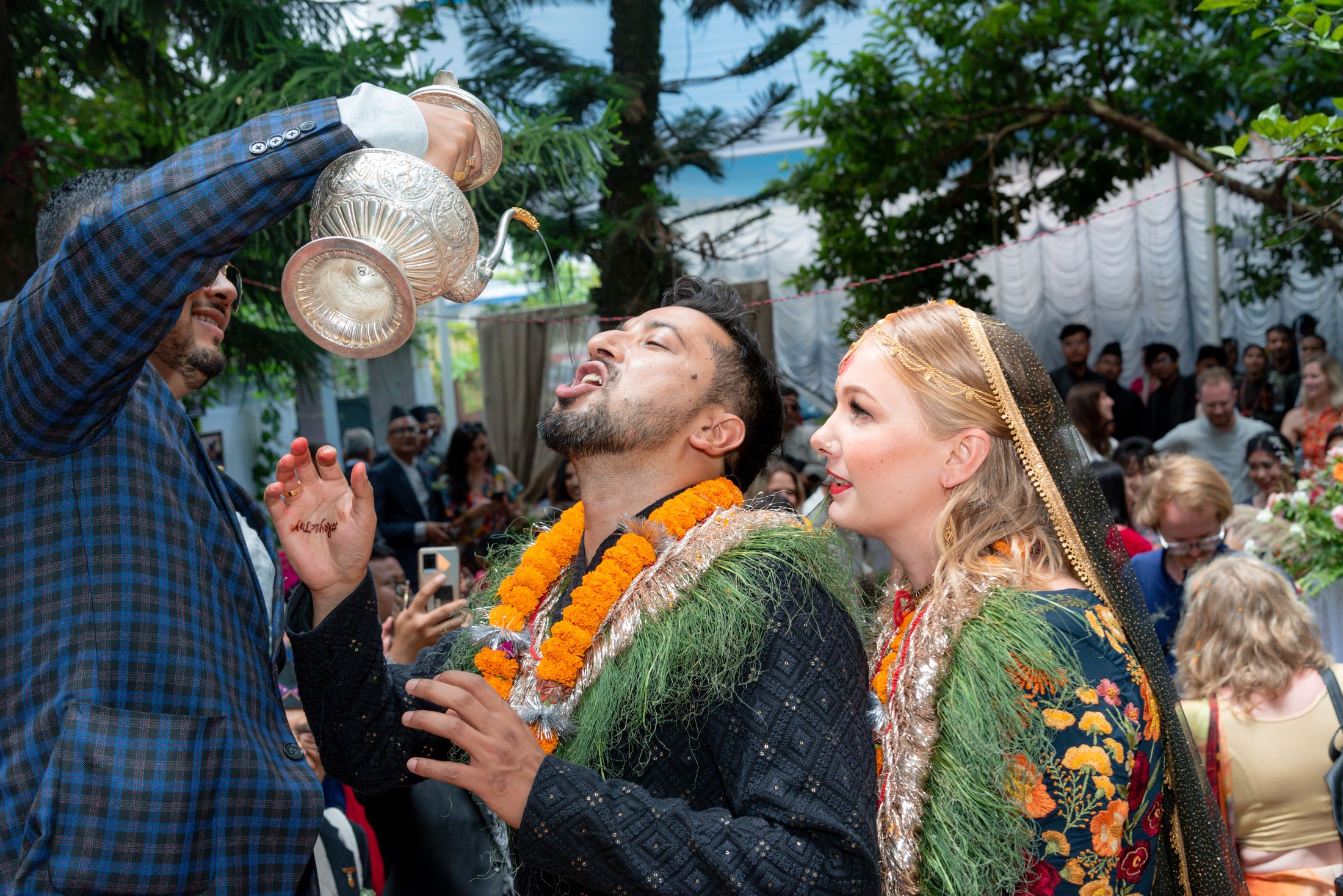 An elder in a grey suit and Nepali topi showering flower petals over Jana and Raymon