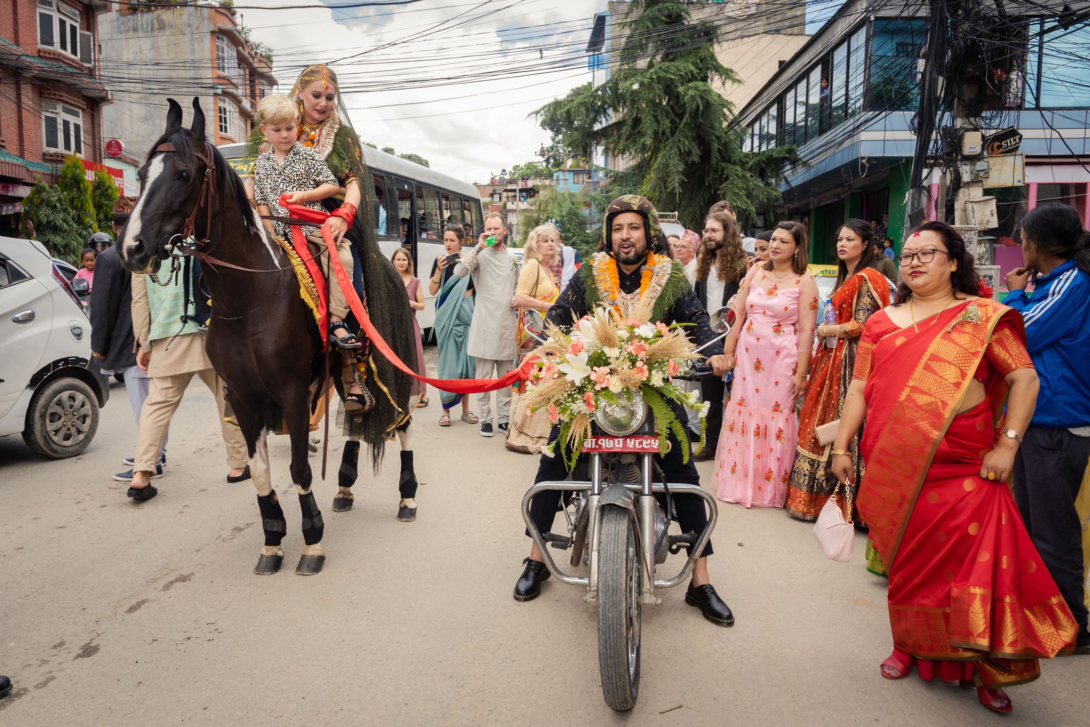 Street procession with Jana riding a decorated horse and Raymon walking beside a flower-adorned scooter