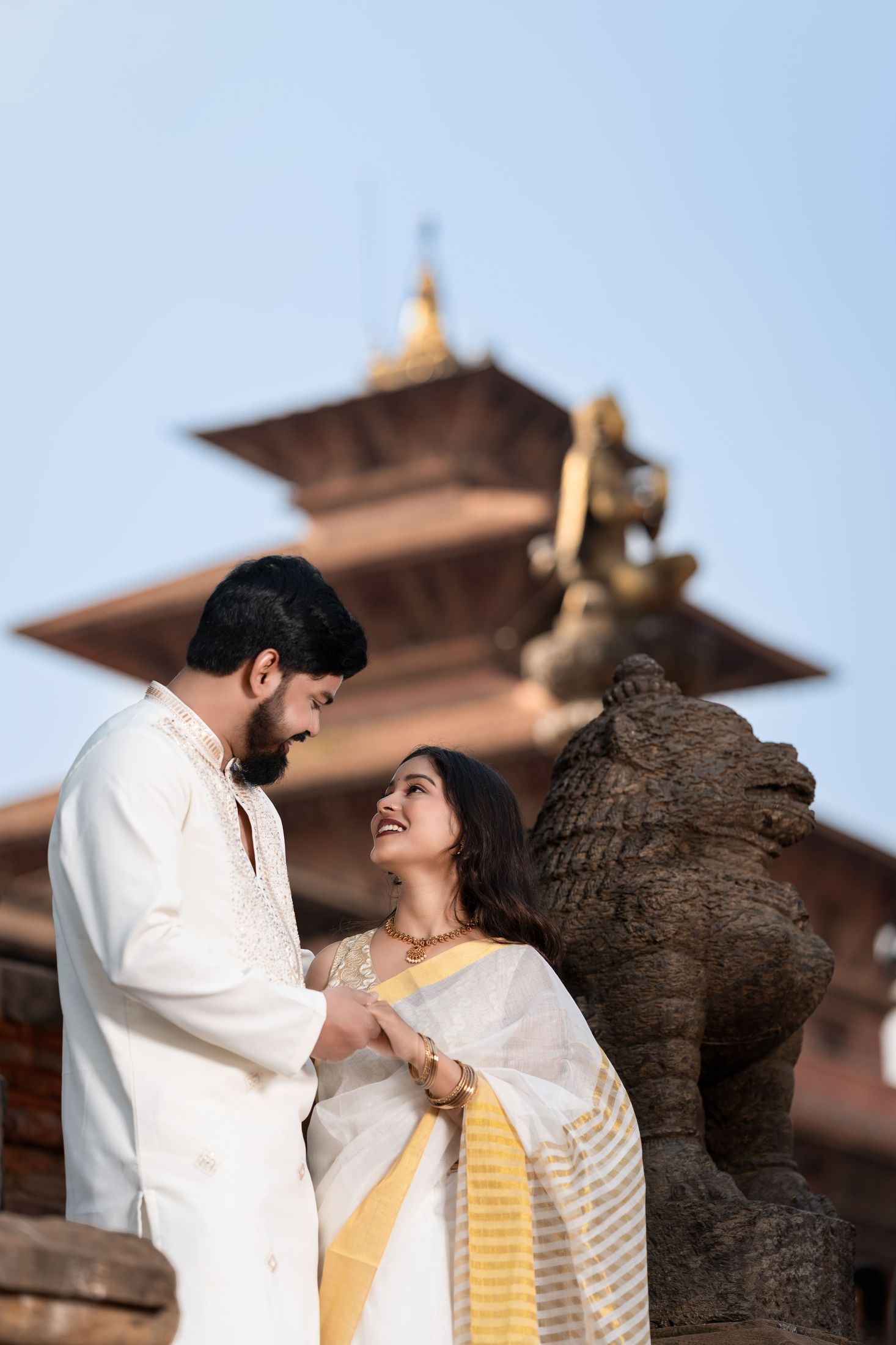 Bride and groom smiling at each other beside a stone lion statue at a Kathmandu temple courtyard