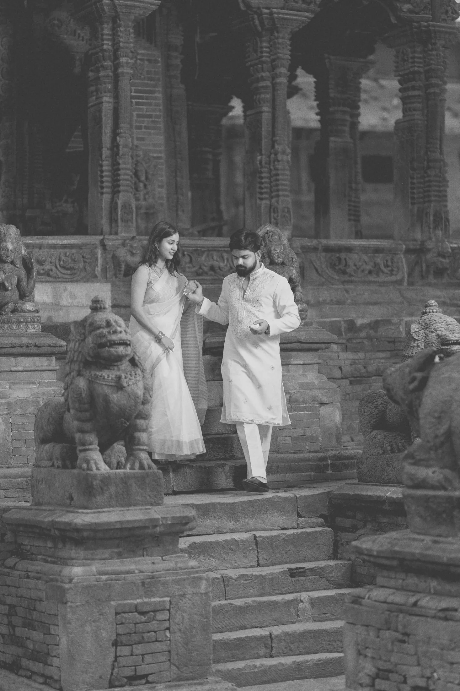 Black and white photo of Jyoti and Rishabh walking down temple steps flanked by stone lion statues