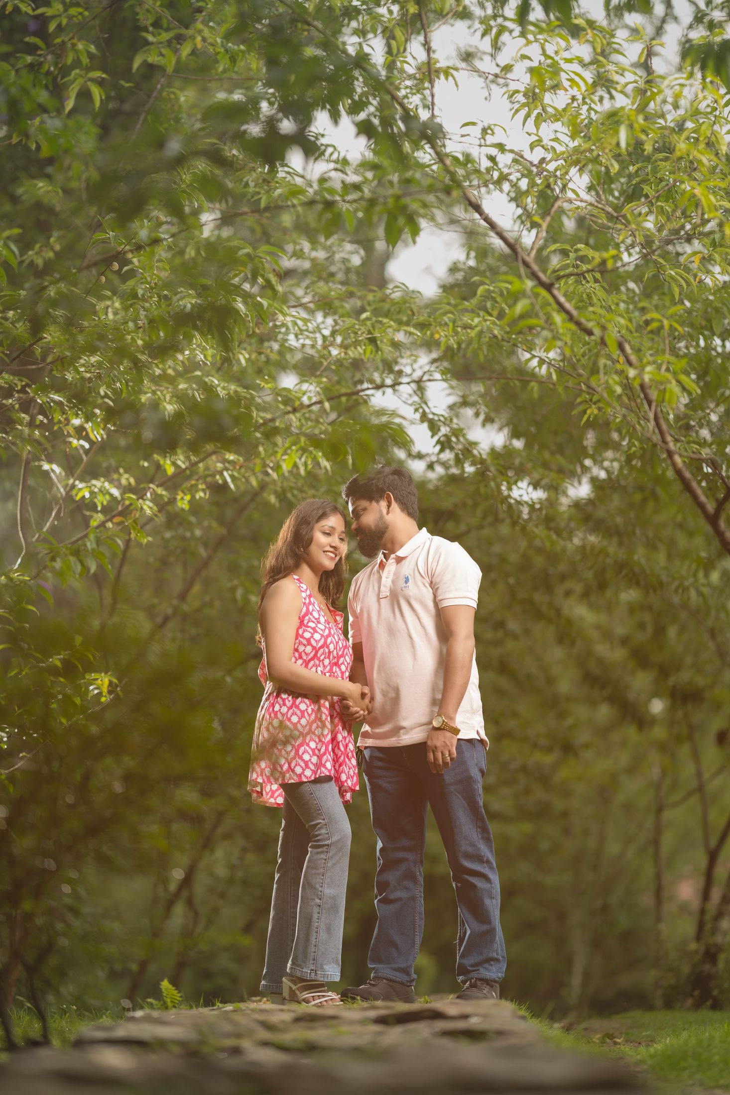 Bride and groom in pink and white outfits smiling together in a green forest