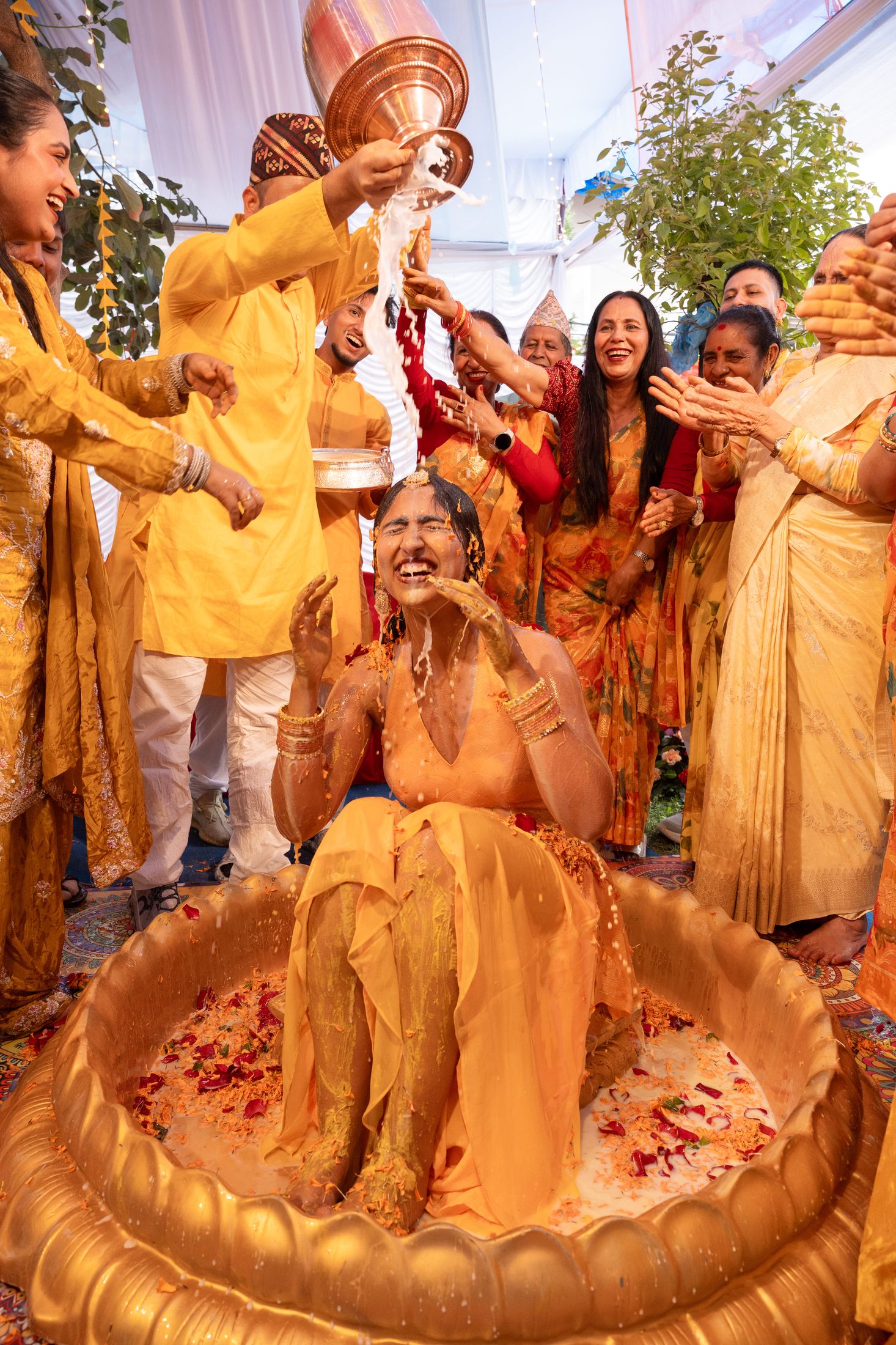 Krishna seated in a golden basin having turmeric poured over him by family members during his haldi ceremony