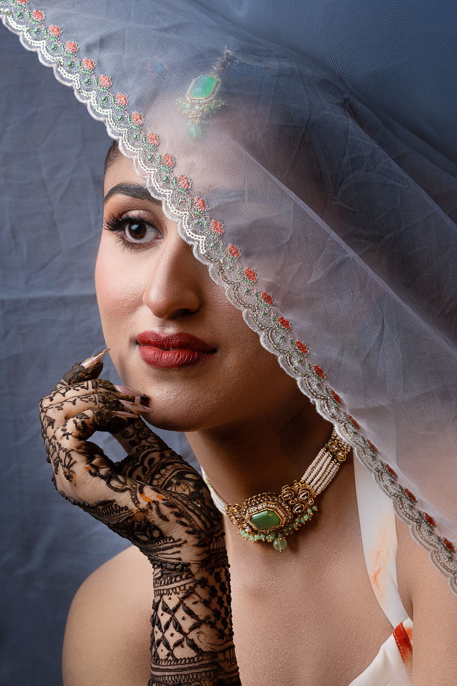 Close-up bridal portrait of Disuja in a veil with henna-covered hands near her face