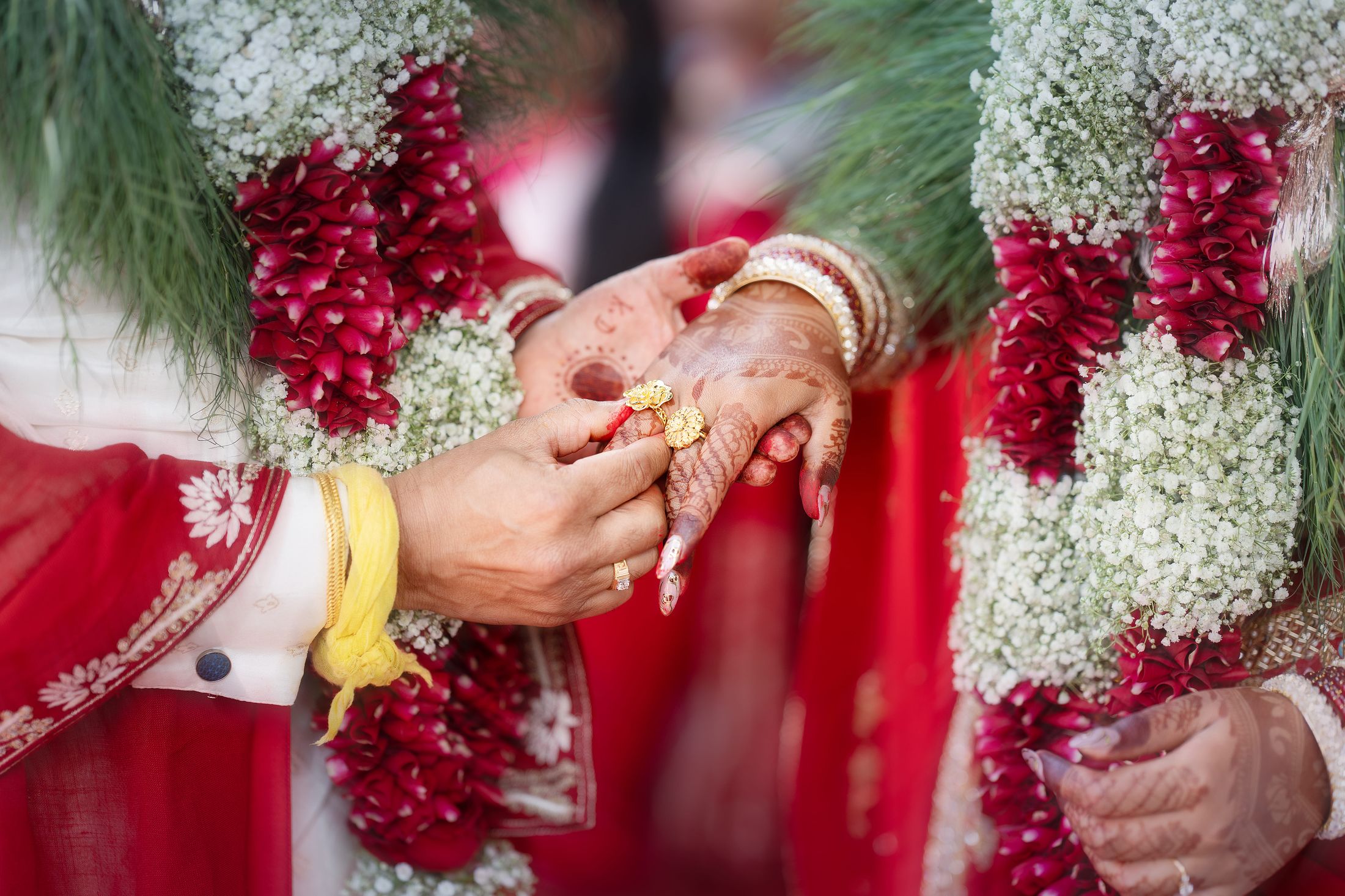 Close-up of the couple's hands exchanging a ring amid rose and baby's breath garlands