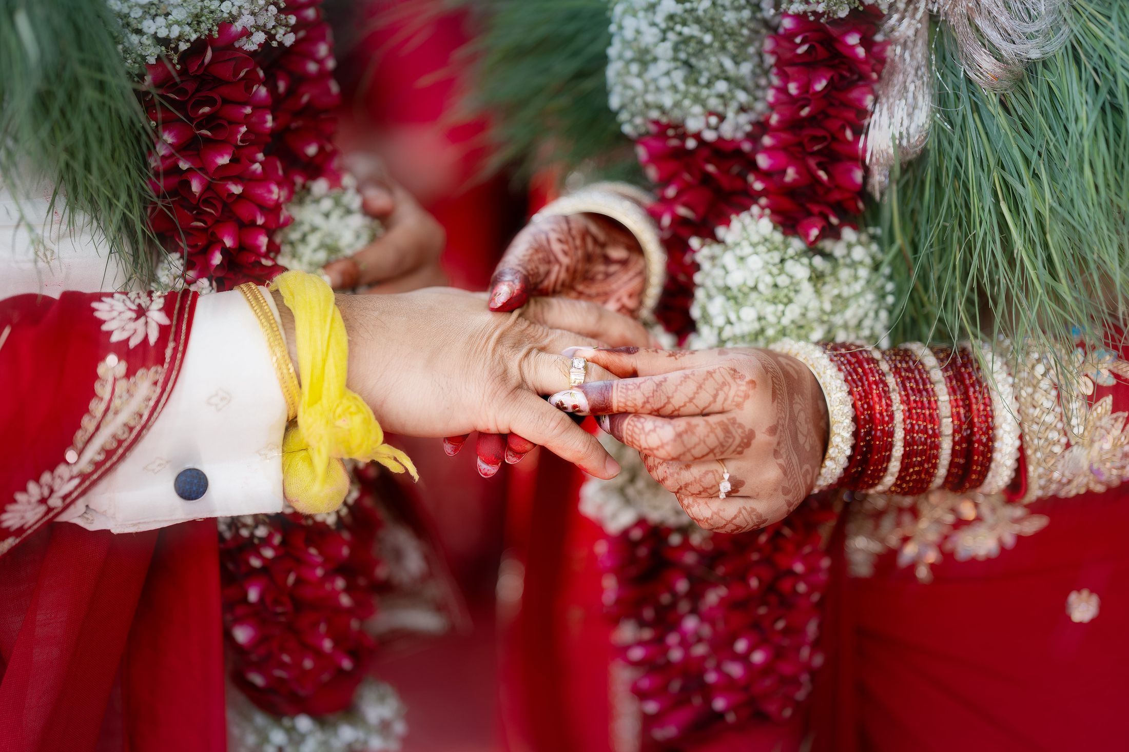Close-up of the couple's hands during the ring ceremony, a different angle of the same garlanded moment