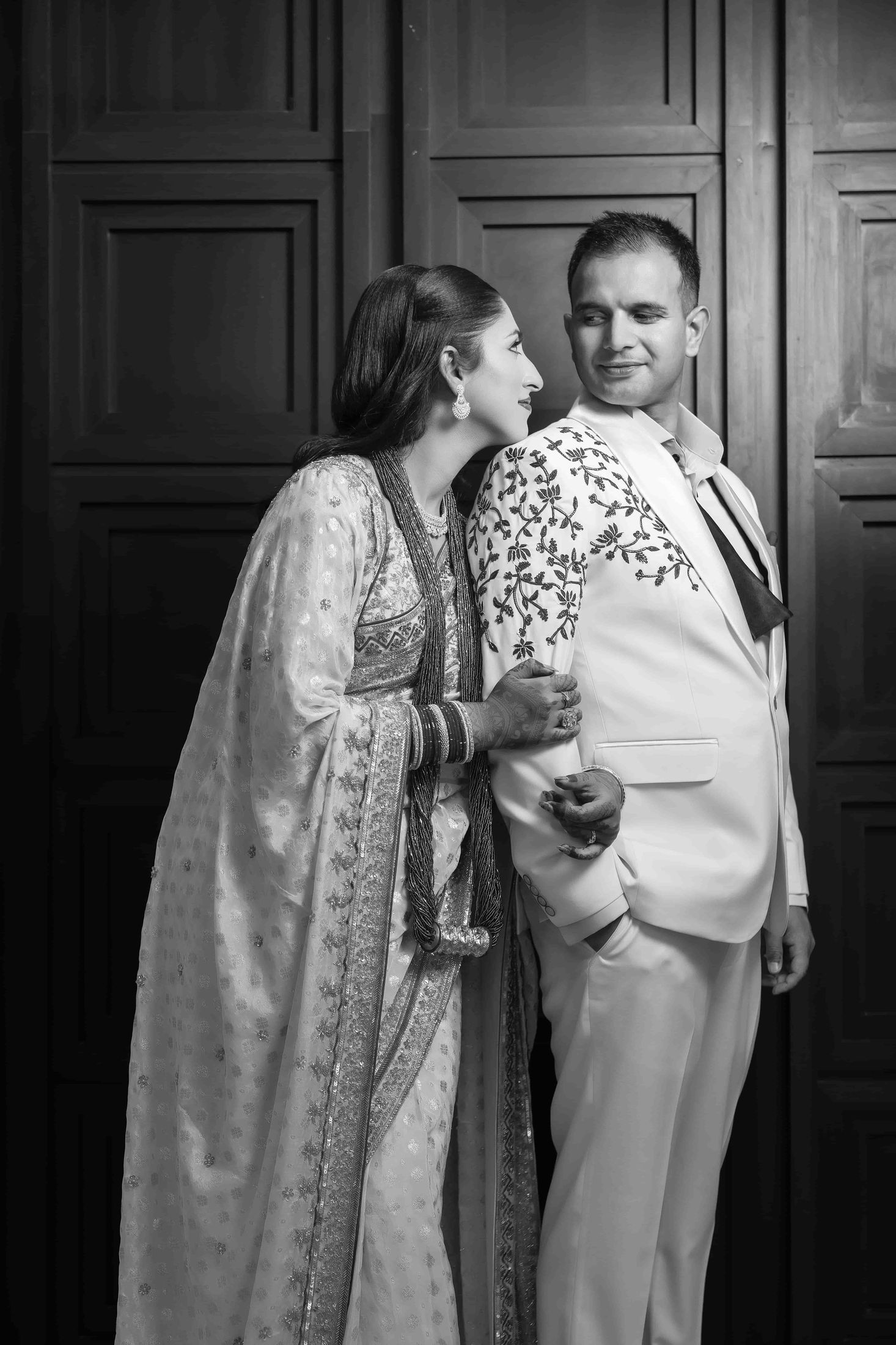 Black and white photo of Disuja resting her head on Krishna's shoulder in front of a carved wooden door