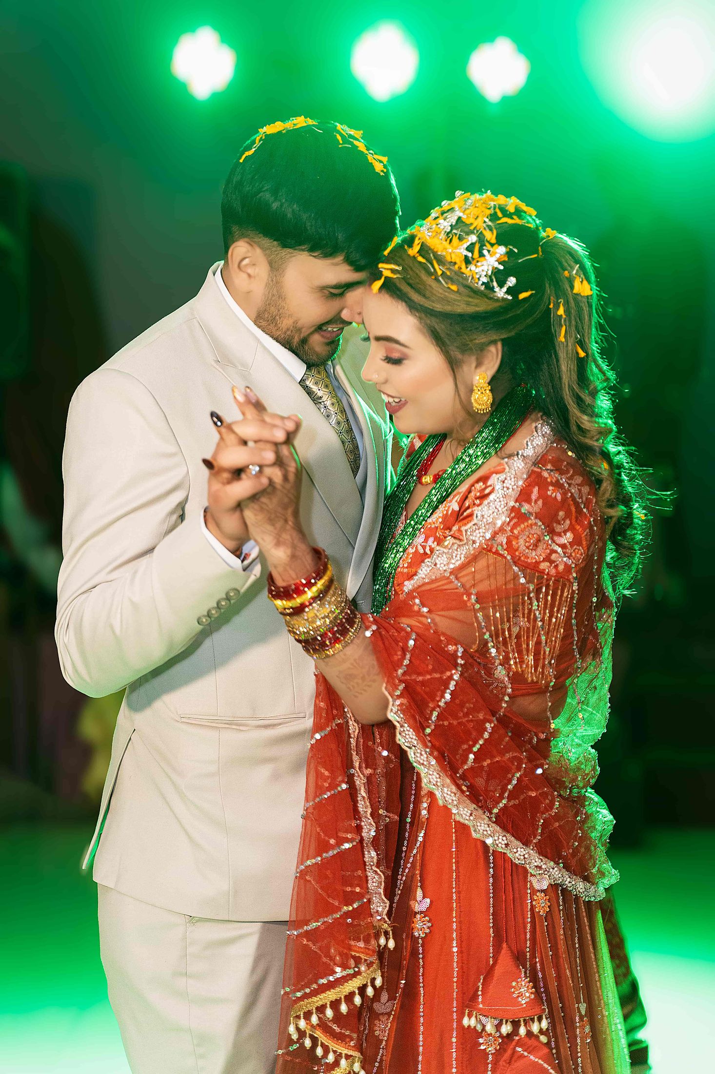 Kristina and Sujan in red and gold wedding attire, foreheads touching tenderly under green stage lighting