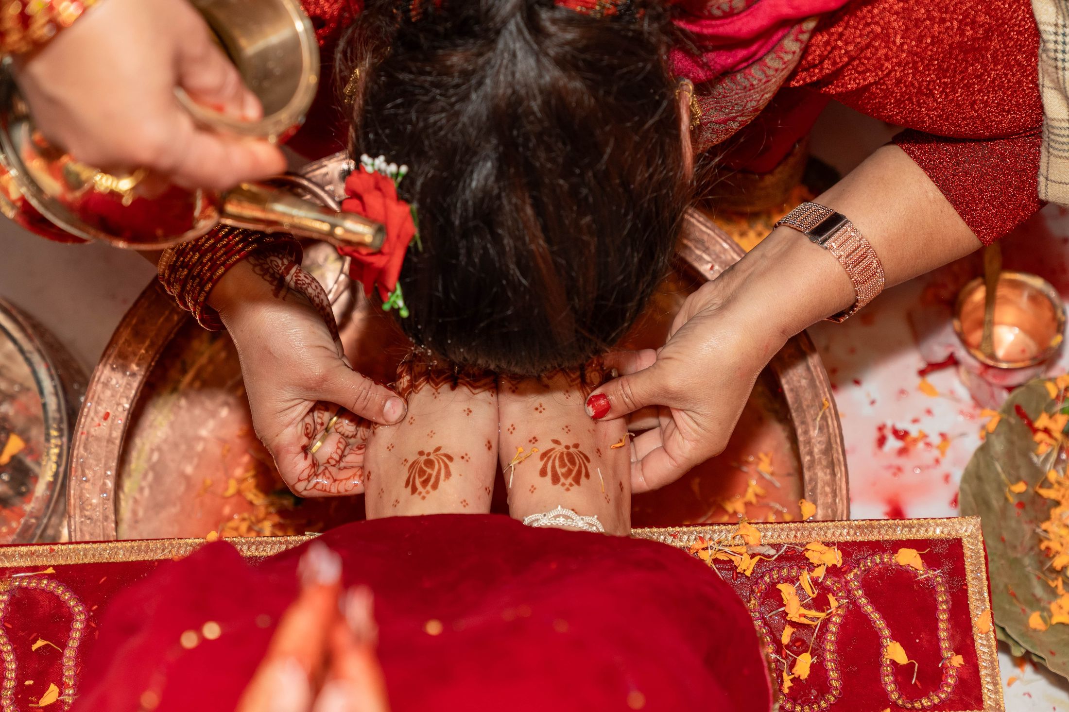 Overhead view of water being poured over Inusha's folded hands during a ritual, she seated in red