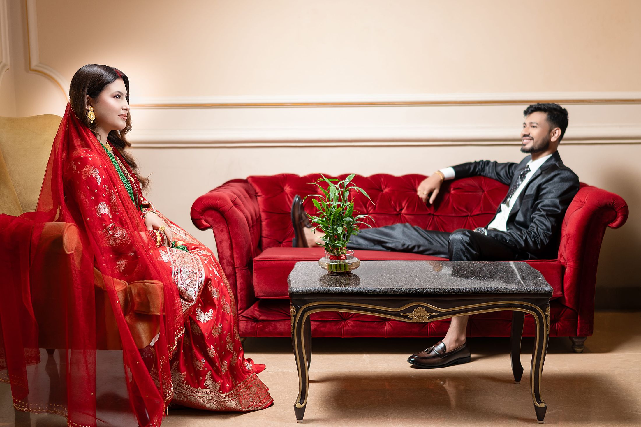 Inusha and Prashid seated across from each other on a red vintage-style sofa