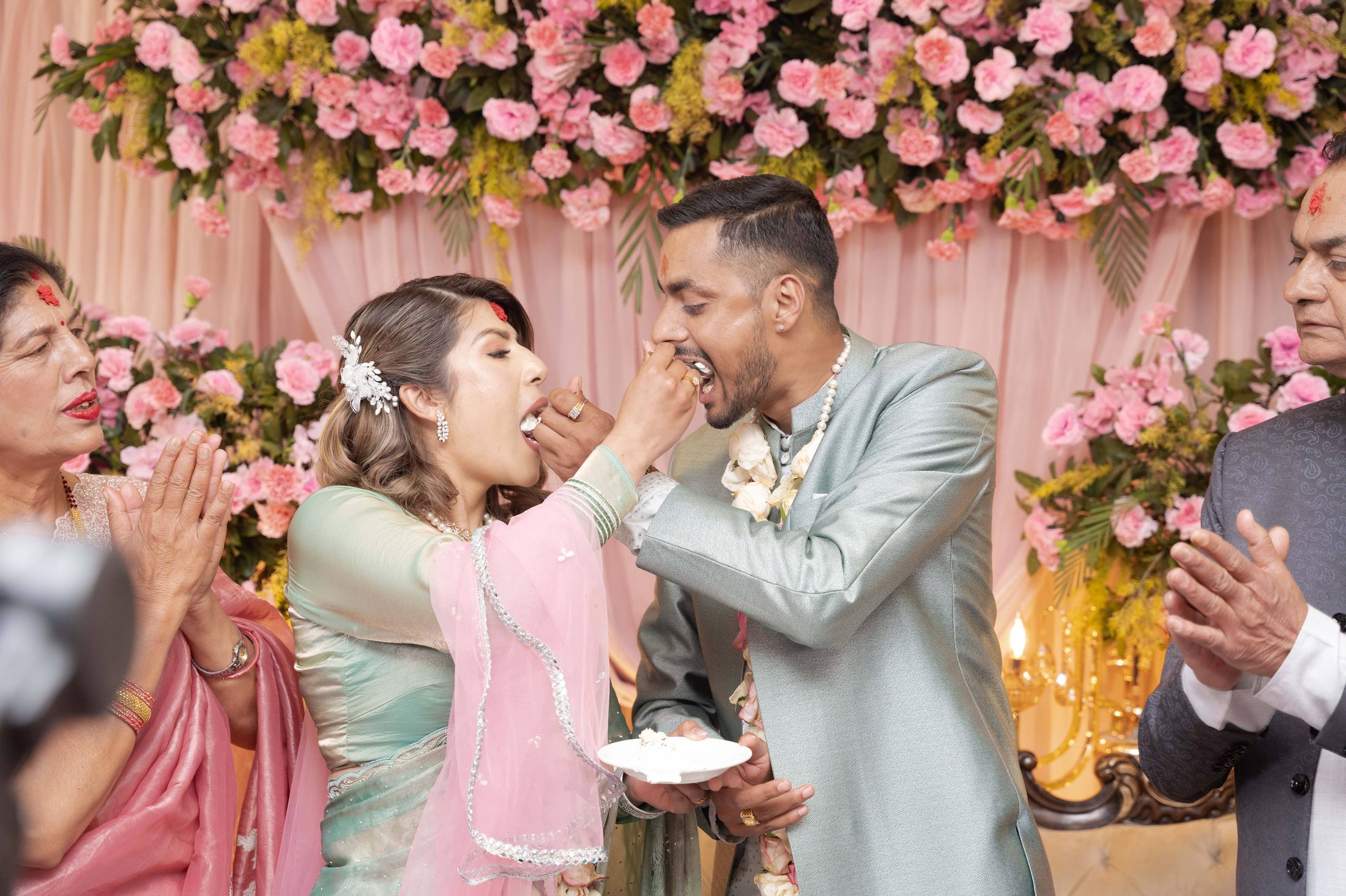 Suprabha and Nischal feeding each other cake as family members give blessings around them