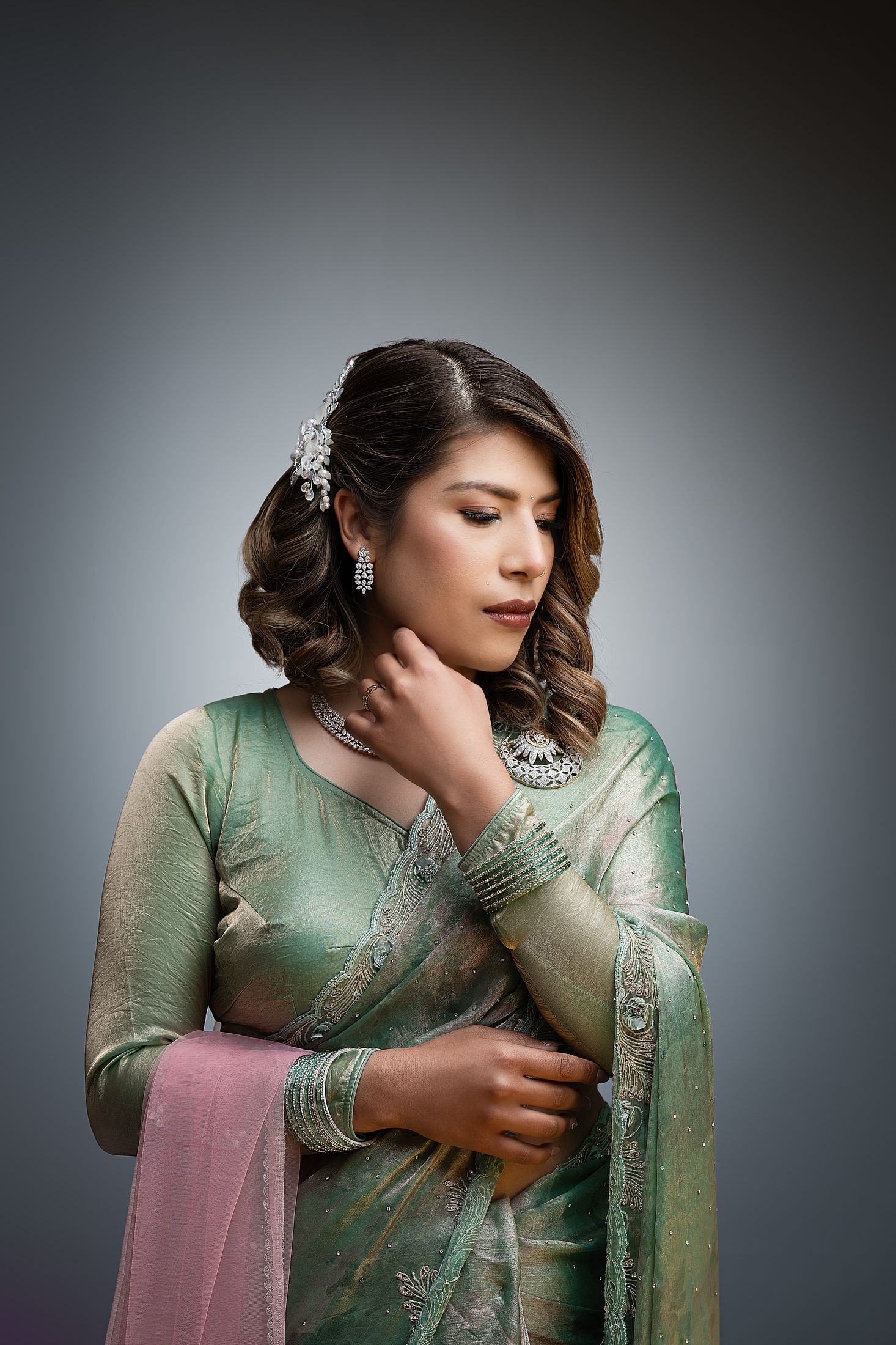 Suprabha in a moody studio portrait touching her necklace against a soft grey background