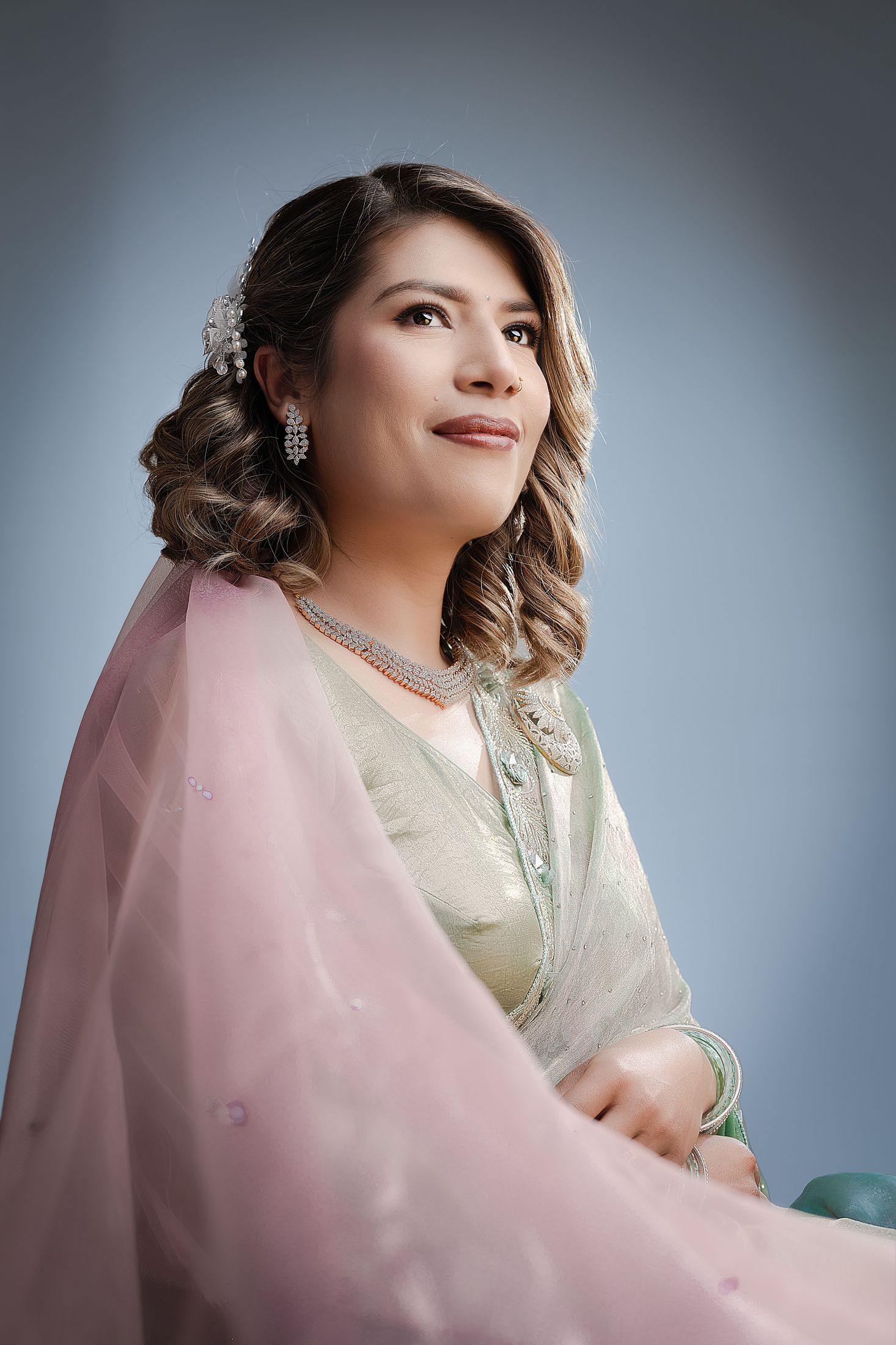 Suprabha in a solo portrait wearing a pink dupatta with curled hair against a soft grey studio background