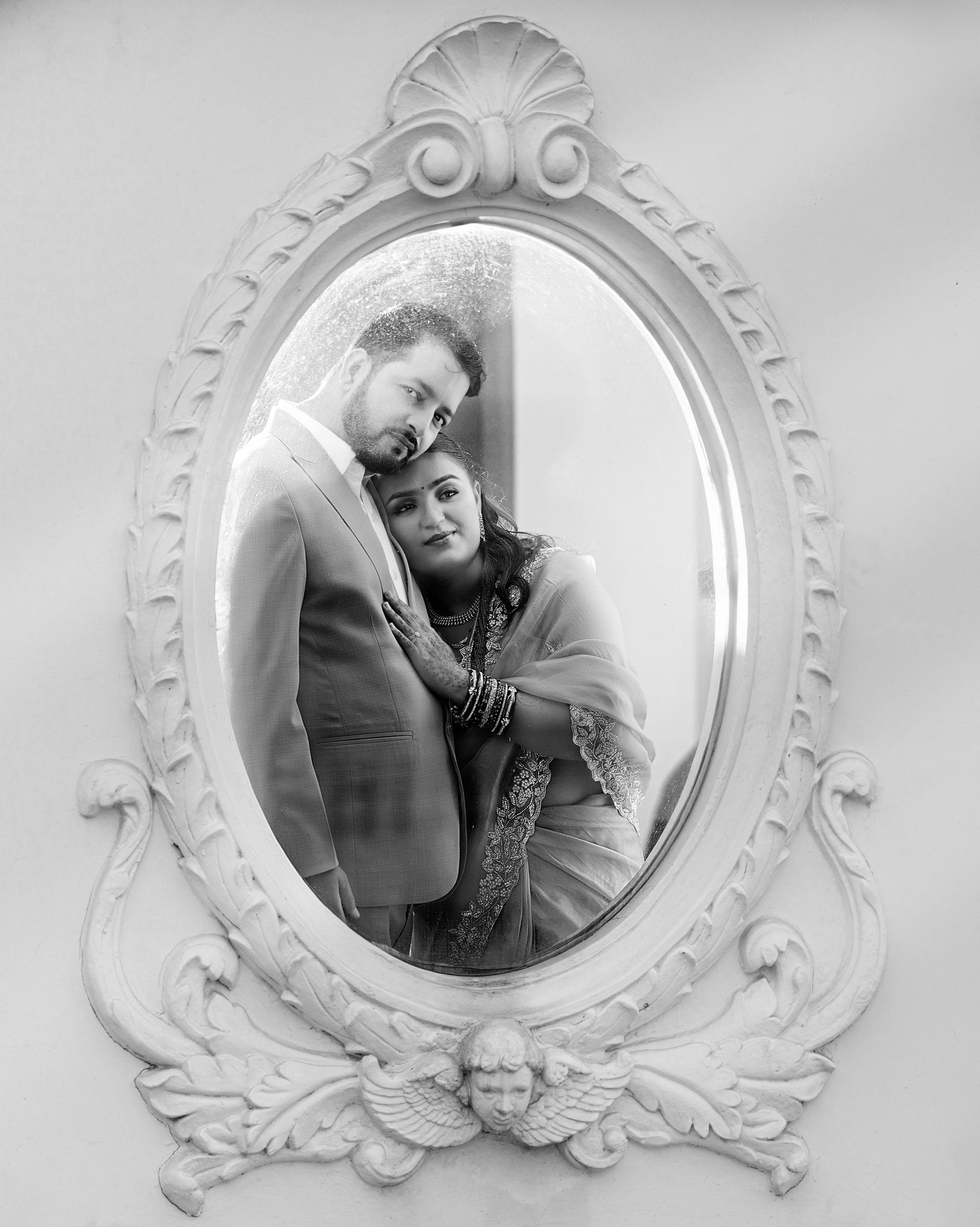 Black and white photo of Sapana and Resham embracing, shown within an ornate oval mirror frame design