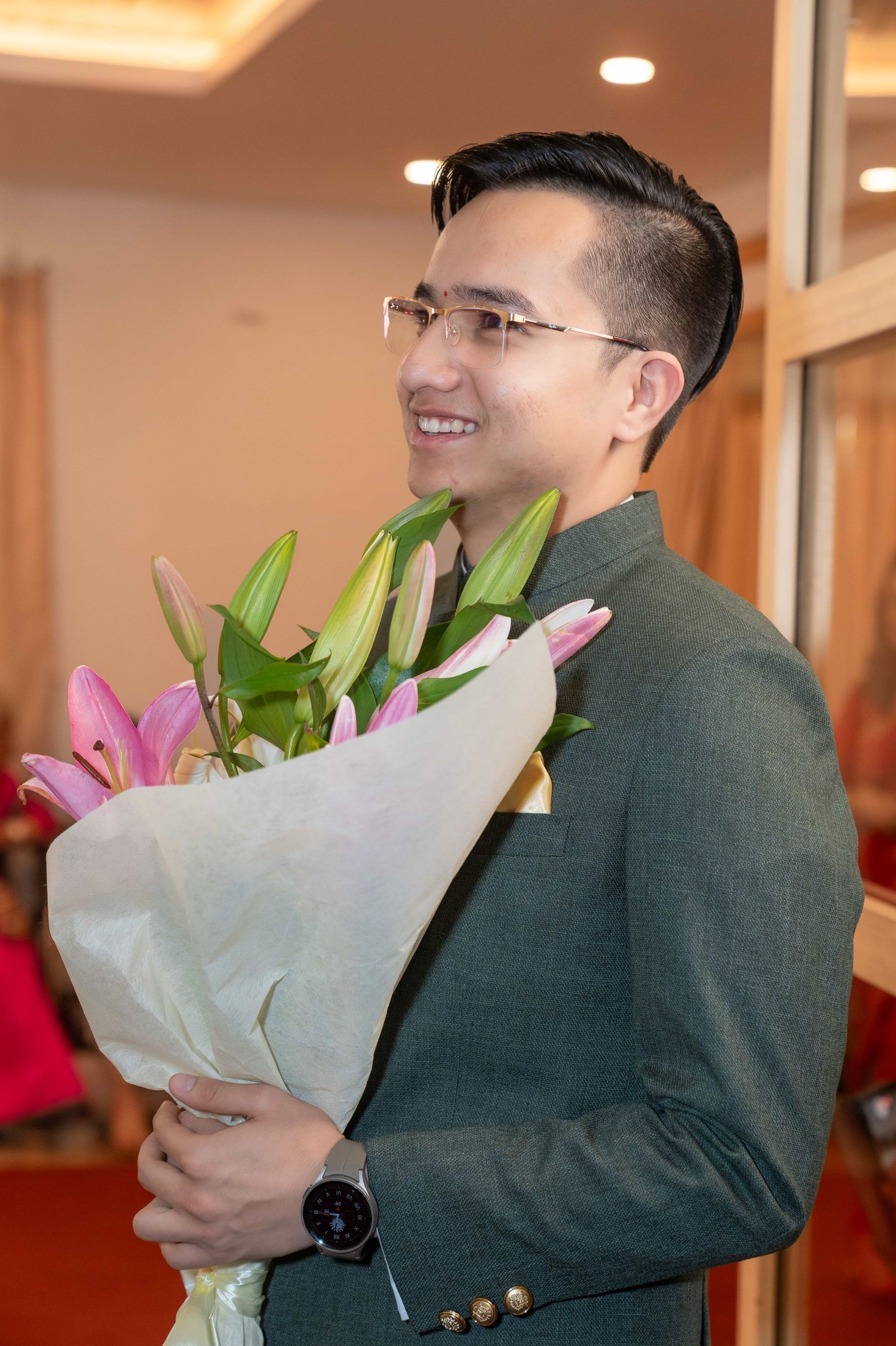 Samagya smiling and holding a pink and white lily bouquet while wearing a floral garland