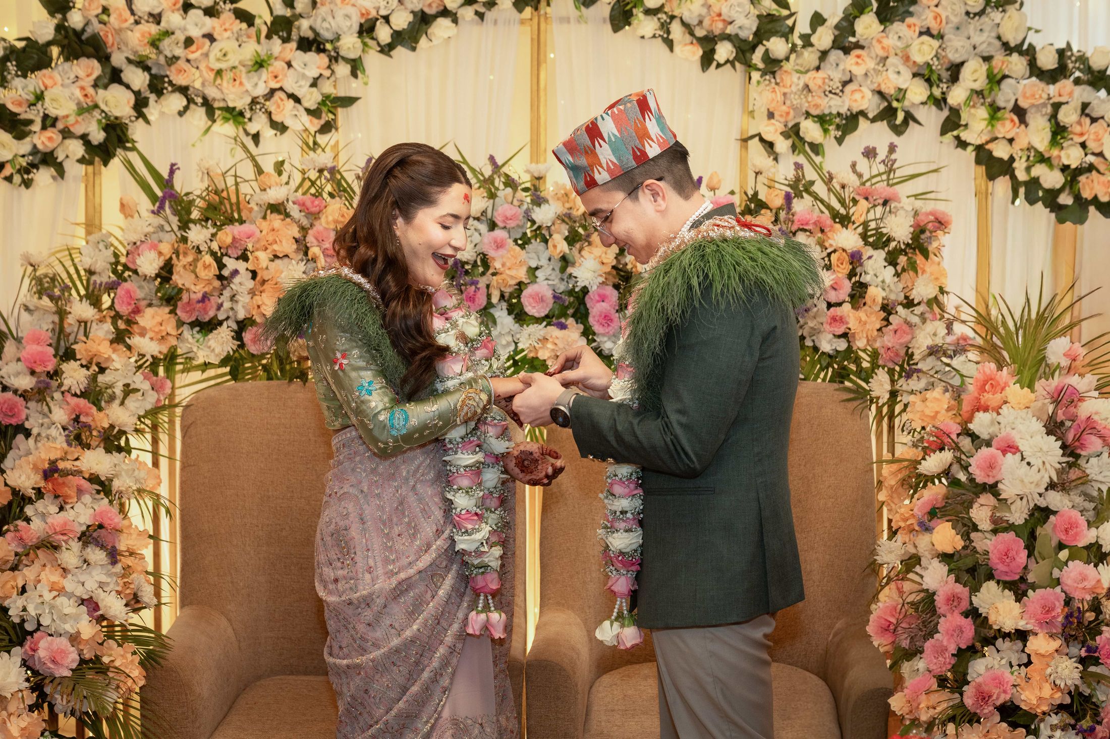Samagya in a traditional Nepali dhaka topi placing a ring on Shreya's finger under the floral arch