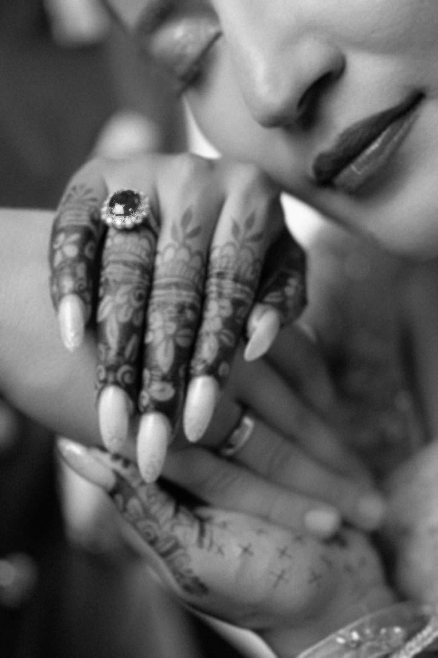 Black and white close-up of Shreya's hennaed hand resting near her face, showing her ring